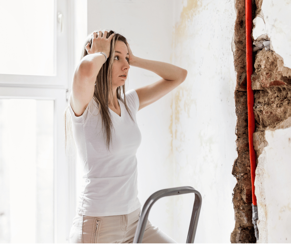 a woman looking at damage caused by a leaking water pipe in a wall